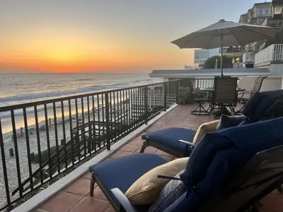 a balcony with chairs and an umbrella and the ocean at Oceanfront 2BR Condo, Private Beach & Patio, Rare Find in Carlsbad