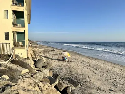 a beach with a building and a person with an umbrella at Oceanfront 2BR Condo, Private Beach & Patio, Rare Find in Carlsbad