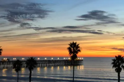 a beach with palm trees and a pier at sunset at Pacific Sunset San Miguel 16 in Oceanside