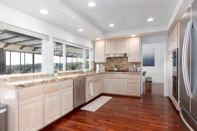 a kitchen with white cabinets and wood floors and windows at Vacation Oasis! Ocean Views~Mini Golf~King-Suites in Solana Beach