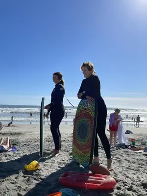 two women standing on the beach with a surfboard at 211A Freshly Renovated Steps from the Sand at the Beach Oceanside in Oceanside