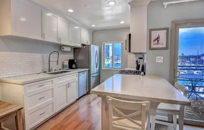 a kitchen with white cabinets and a kitchen island with a table at 307B Steps from the sand! Freshly Decorated with Harbor Views in Oceanside