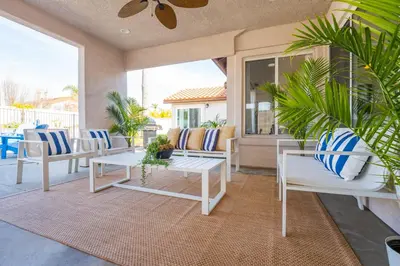 a porch with white chairs and tables and plants at Luxury poolside « Villa Descanso » with heated pool and Spa! Close to San Diego/ Legoland in Oceanside