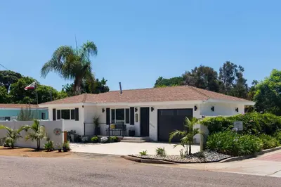a white house with a fence and palm trees at Coasta Casa, Retreat by the Sea. E-Charger. in Carlsbad