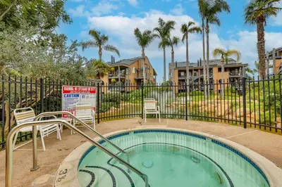 a pool with chairs and a fence with palm trees at Carlsbad Rental with Private Balcony and Pool Access! in Carlsbad