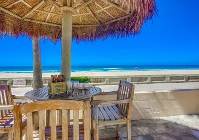a table and chairs under a straw umbrella on the beach at Aloha Breeze 1 in San Diego