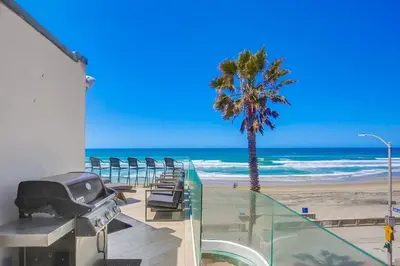a beach with chairs and a grill and a palm tree at Beachside 2 in San Diego