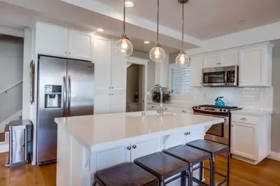 a kitchen with white cabinets and a large island with bar stools at Cali Vibes in San Diego