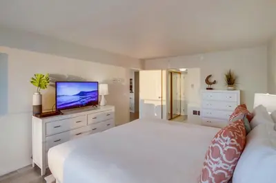 a bedroom with a white bed and a flat screen tv at Capri by the Sea in San Diego