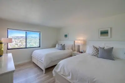 a white bedroom with two beds and a window at Capri by the Sea in San Diego
