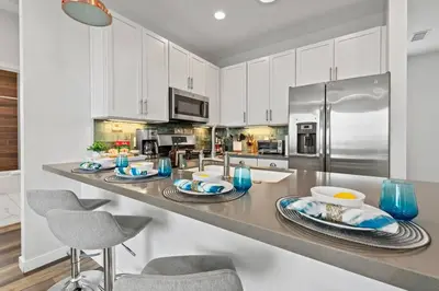 a kitchen with white cabinets and a stainless steel refrigerator at Saratoga Sunset - Rooftop - Sleek - Walk to Beach in San Diego