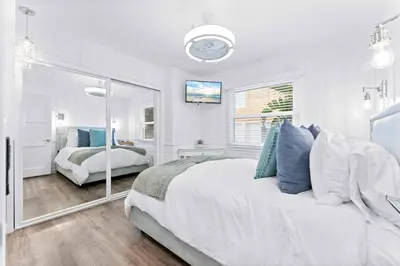 a white bedroom with a large bed and a mirror at Magical Bayfront Home w Epic Dock on Peninsula in Newport Beach