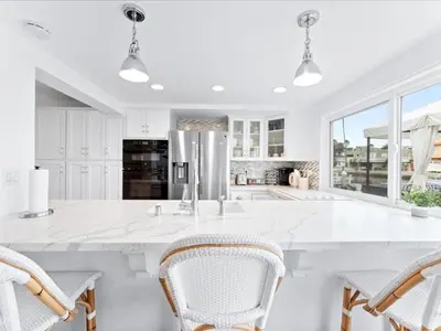 a white kitchen with a large white island with chairs at Stunning Bayfront Home w Epic Dock on Peninsula in Newport Beach