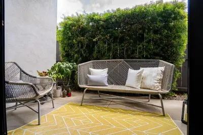 a wicker bench sitting on a patio with two chairs at Bright Designer Oasis - Block from Bay - Roof Deck in San Diego