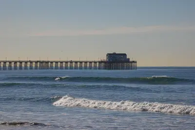 a pier in the ocean with a surfer in the water at Oceanside Beach Condos in Oceanside