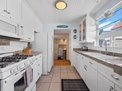 a kitchen with white cabinets and a stove and sink at Stunning beach home - steps2sand, AC, Large Patio and Fast Wifi! in San Diego