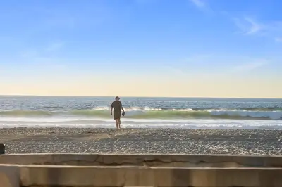 a person standing on the beach with a surfboard at Beautiful Beach Home - Ocean View, AC & Patio in San Diego