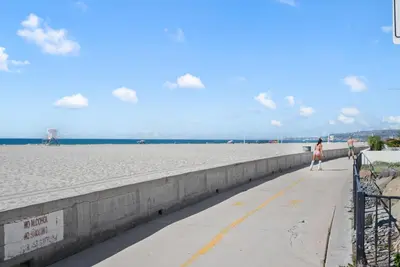 a woman walking down a sidewalk next to the beach at Ocean View Paradise w Private Patio & Spa in San Diego