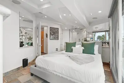 a white bedroom with a large bed with green pillows at Stunning Oceanfront Boardwalk Condo - Spa, Steps2Beach, Parking & Fast Wifi! in San Diego