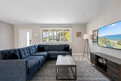a living room with a blue couch and a flat screen tv at Bird Rock Dreams - Ocean Views, Massive Yard, Outdoor Dining, Fast Wifi & AC! in San Diego