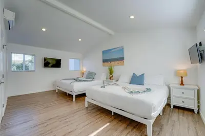 two beds in a room with white walls and wooden floors at Shores Perfection - Spa, AC, Pet Friendly, Parking, Fire Pit & Massive Private Yard! in San Diego