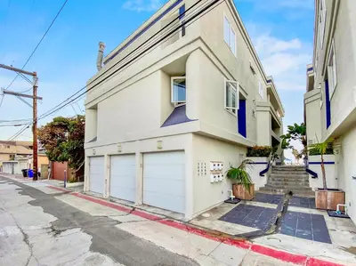 a white house with two garage doors on a street at Oceanfront Condo with Front Patio, Gas Grill, Fire Pit - Prime Location!! in San Diego