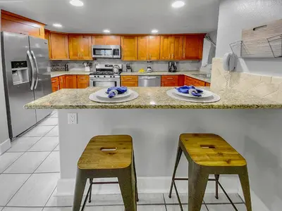 a kitchen with a counter with two stools and a refrigerator at Oceanfront Condo with Front Patio, Gas Grill, Fire Pit - Prime Location!! in San Diego