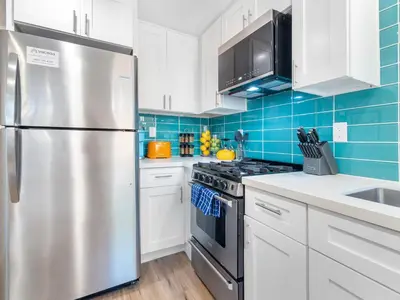 a kitchen with white cabinets and a stainless steel refrigerator at Beach Bungalow Perfection - Private Patios, BBQ walk2beach & Pet Friendly! in San Diego