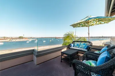 a balcony with chairs and an umbrella and a beach at Bayfront Dream - Bay Views, Rooftop Patio, & Garage! in San Diego