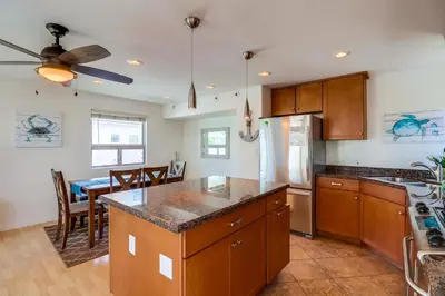 a kitchen with wooden cabinets and a dining room at Beach Oasis - Rooftop, Steps2Sand and Water Views in San Diego