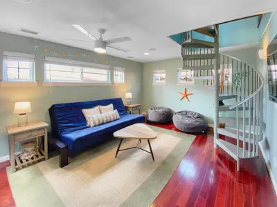 a living room with a blue couch and a spiral staircase at Massive Mission Beach Home - Fire Pit & Deck in San Diego