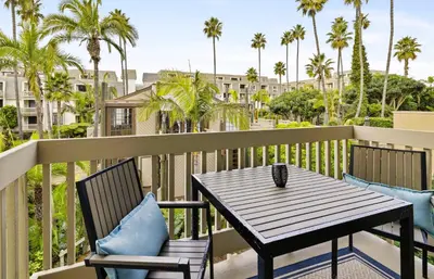 a table and chairs on a balcony with palm trees at Brooks Beach Vacations Villa C205 Oceanside in Oceanside