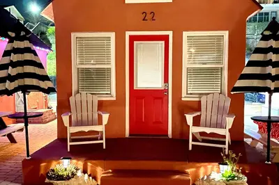 a house with a red door and two white chairs at Sandcastle Cottage 22 in Oceanside