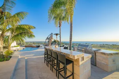 a patio with a bar and a grill and palm trees at Ocean View Serenity with Theater and Heated Pool in San Diego