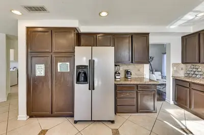 a kitchen with a refrigerator and wooden cabinets at Lake Elsinore Home with Pool - 44 Mi to Disneyland! in Lake Elsinore