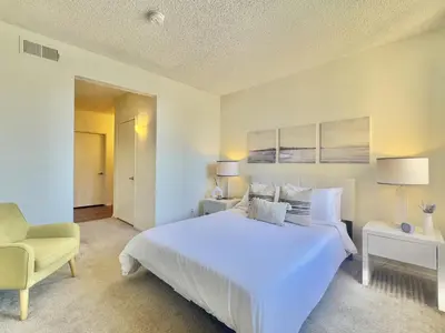 a white bedroom with a large bed and a chair at SPECIAL OFFER - Modern Apartment in La Jolla UTC - Close to Beaches, Shopping, Dining, UCSD in San Diego