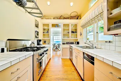 a kitchen with white cabinets and a wooden floor at Oceanfront Dog Friendly Home with Waterfront Porch, Gas Grill, Hot Tub & Fire Pit in San Diego