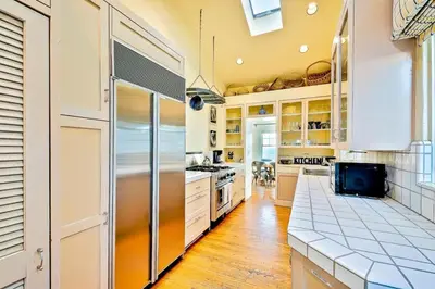 a kitchen with white cabinets and a stainless steel refrigerator at Oceanfront Dog Friendly Home with Waterfront Porch, Gas Grill, Hot Tub & Fire Pit in San Diego