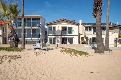 a house on the beach with two chairs and palm trees at Oceanfront Home with UNOBSTRUCTED VIEW in Newport Beach
