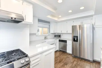 a kitchen with white cabinets and a stainless steel refrigerator at 5 Bedroom Home with Pool Table steps to the Beach in Newport Beach