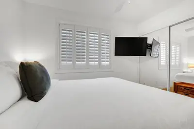 a white bedroom with a white bed and a television at Fantastic bayside vacation home - WiFi, central AC, patio, private washer & dryer in San Diego
