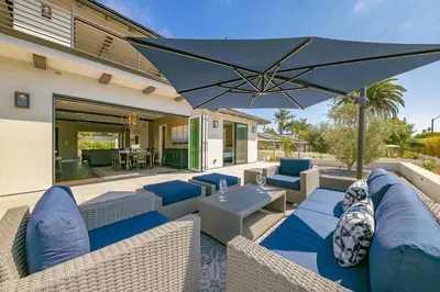 a patio with blue chairs and an umbrella at Luxury Bird Rock Home with Private Pool, Hot Tub & Fire Pit! in San Diego