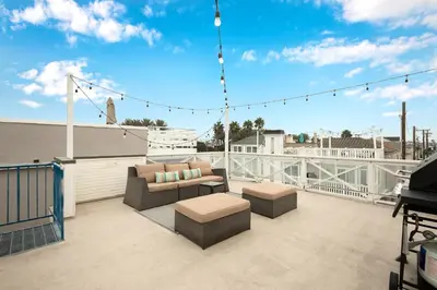 a patio with a couch and tables on a balcony at 7 Bedroom Duplex Home with Rooftop & Peek-A-Boo Ocean View in Newport Beach