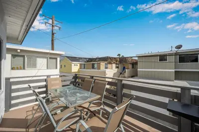 a patio with chairs and a glass table on a balcony at 2 Bedroom Upstairs with Balcony Steps from the Sand in Newport Beach