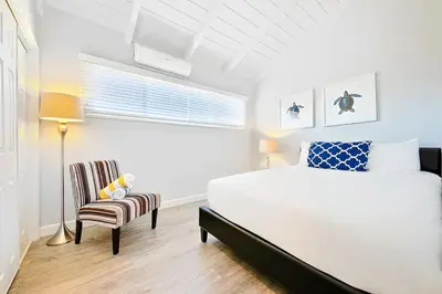 a white bedroom with a bed and a chair at Duplex Across the Street from Beach & Boardwalk in Newport Beach