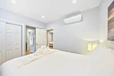 a white bedroom with a large white bed and a fan at Duplex Across the Street from Beach & Boardwalk in Newport Beach