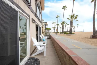 a building with two white chairs on a sidewalk next to the beach at Updated Home on the Boardwalk with Private Rear Unit in Newport Beach