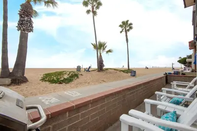 a beach with palm trees and white lounge chairs at Updated Home on the Boardwalk with Private Rear Unit in Newport Beach