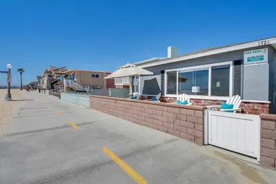 a building with an umbrella and chairs on a sidewalk at TWO BEACHFRONT BUNGALOWS ON THE SAND IN Newport Beach in Newport Beach