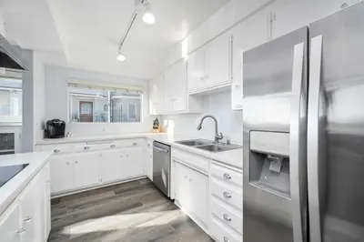 a kitchen with white cabinets and a stainless steel refrigerator at 5 Bedroom Duplex on the Boardwalk next to Balboa Pier in Newport Beach